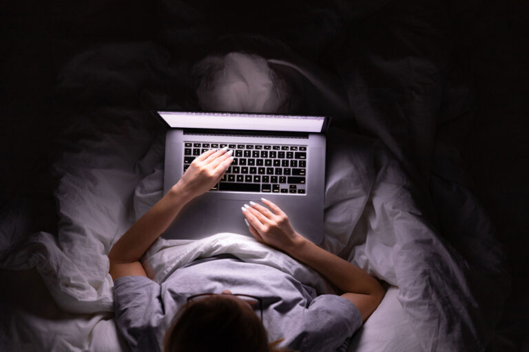 Woman lying in bed working on laptop late at night